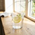 Frisk vand med citronsnegl i glas på solbeskinnet køkkenbord, symboliserer daglig væskeindtag